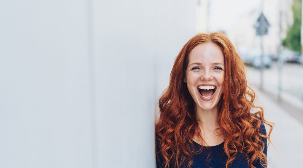 Smiling woman with long red hair showcasing a bright, white smile, embodying the benefits of teeth whitening for springtime in Knoxville.
