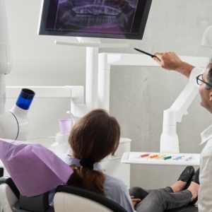 Dentist discussing dental health with patient while pointing at X-ray image on screen in a modern dental office setting.